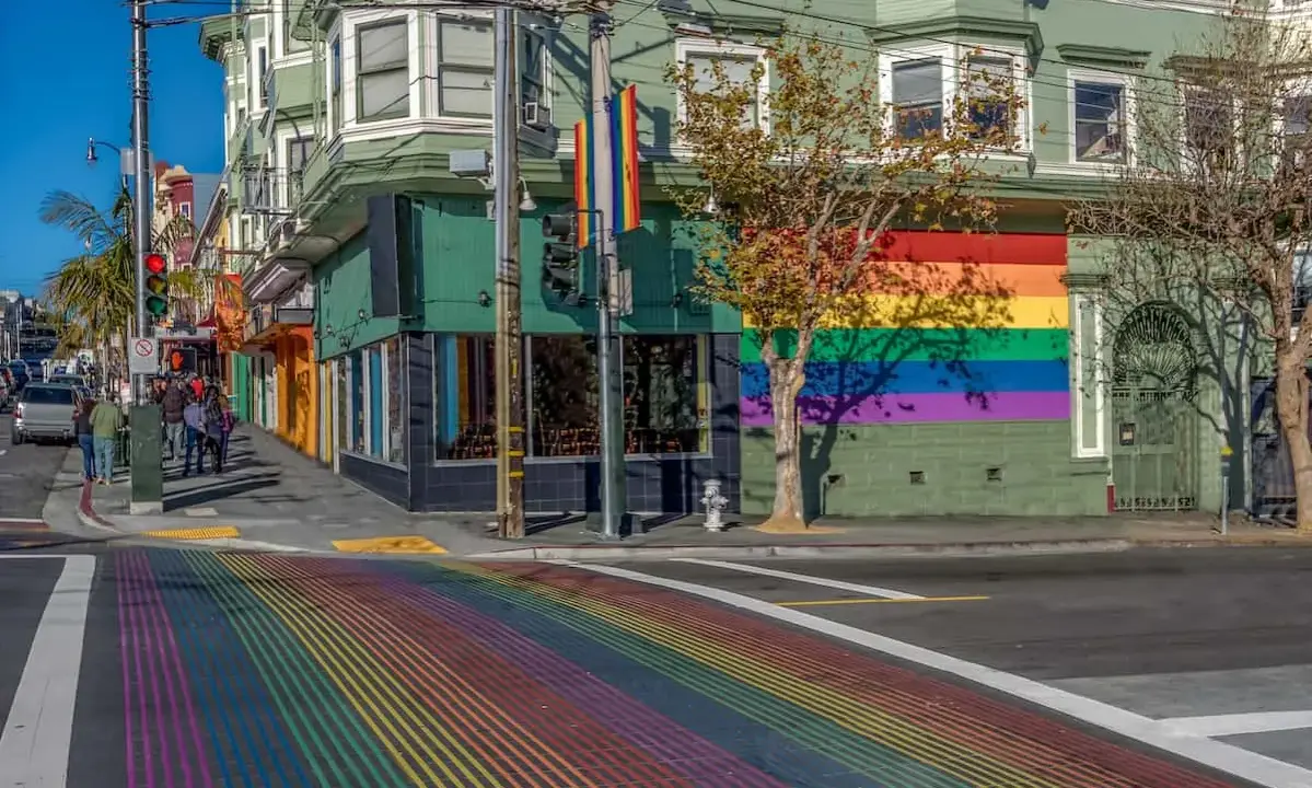 A vibrant rainbow crosswalk leads to a building adorned with a large rainbow mural, a symbol of the gay bed breakfast scene in San Francisco.