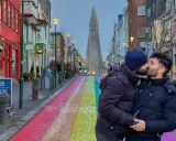 A couple shares a kiss on a rainbow-painted street in gay Reykjavik, with Hallgrímskirkja church in the background.