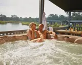 A happy couple enjoys a hot tub with a view of a serene gay lake.