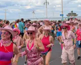 A vibrant Brighton gay pride parade, with many participants wearing pink cowboy hats and rainbow-themed attire, celebrating joyfully by the sea.