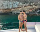 A loving gay couple shares a kiss on a boat, enjoying the stunning scenery of the Canary Islands.