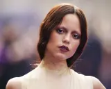 A young woman with auburn hair and a dramatic, dark lipstick looks directly at the camera. Her eye makeup is smudged, giving her a tired girl makeup look, as if she's been out all night.