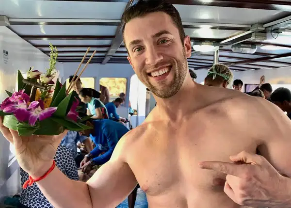Smiling man on a boat in Asia, holding a flower offering. A perfect moment for gay travel in Asia.