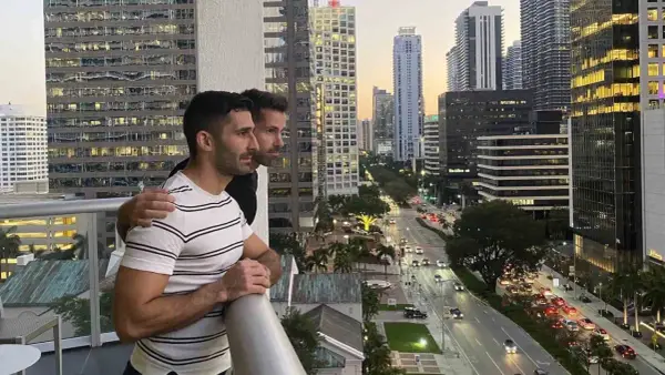 Two men embrace on a balcony overlooking a city street, a scene reminiscent of some of the most gay cities in the US.