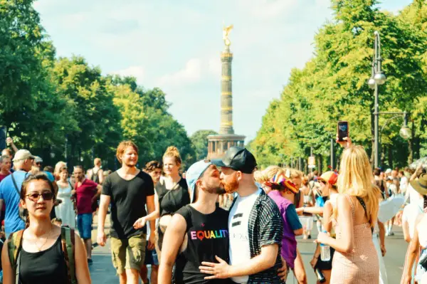 A couple kisses at a pride parade in Germany, with the Victory Column in the background. This scene shows Germany is gay friendly.
