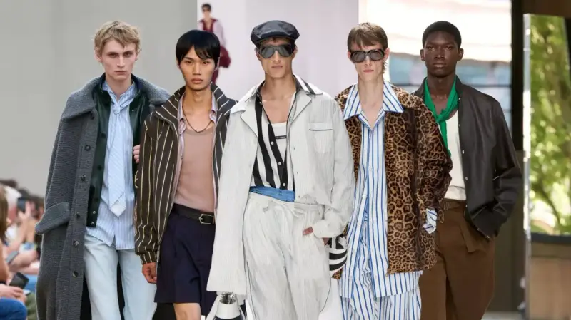 Five models showcase bold gay men fashion on a runway, featuring a mix of stripes, leopard print, and stylish outerwear.